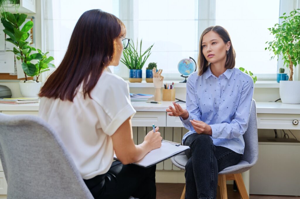 Young woman at a mental therapy session talking to female psychologist in therapist's office. Smiling female patient, help support professional counselor, psychotherapist, mental health youth concept